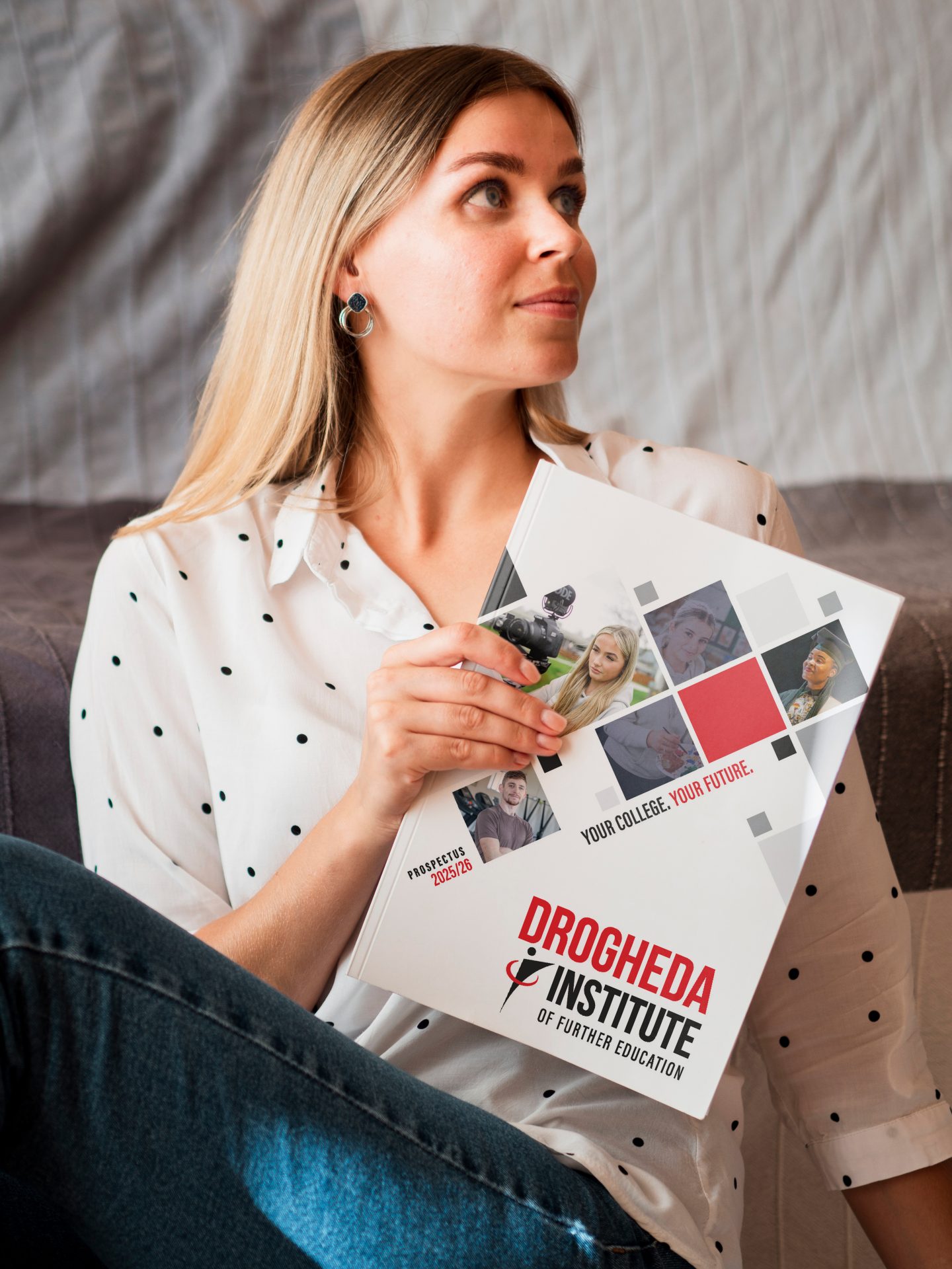 Woman seated on a sofa holding a printed Drogheda Institute of Further Education prospectus with student photos on cover