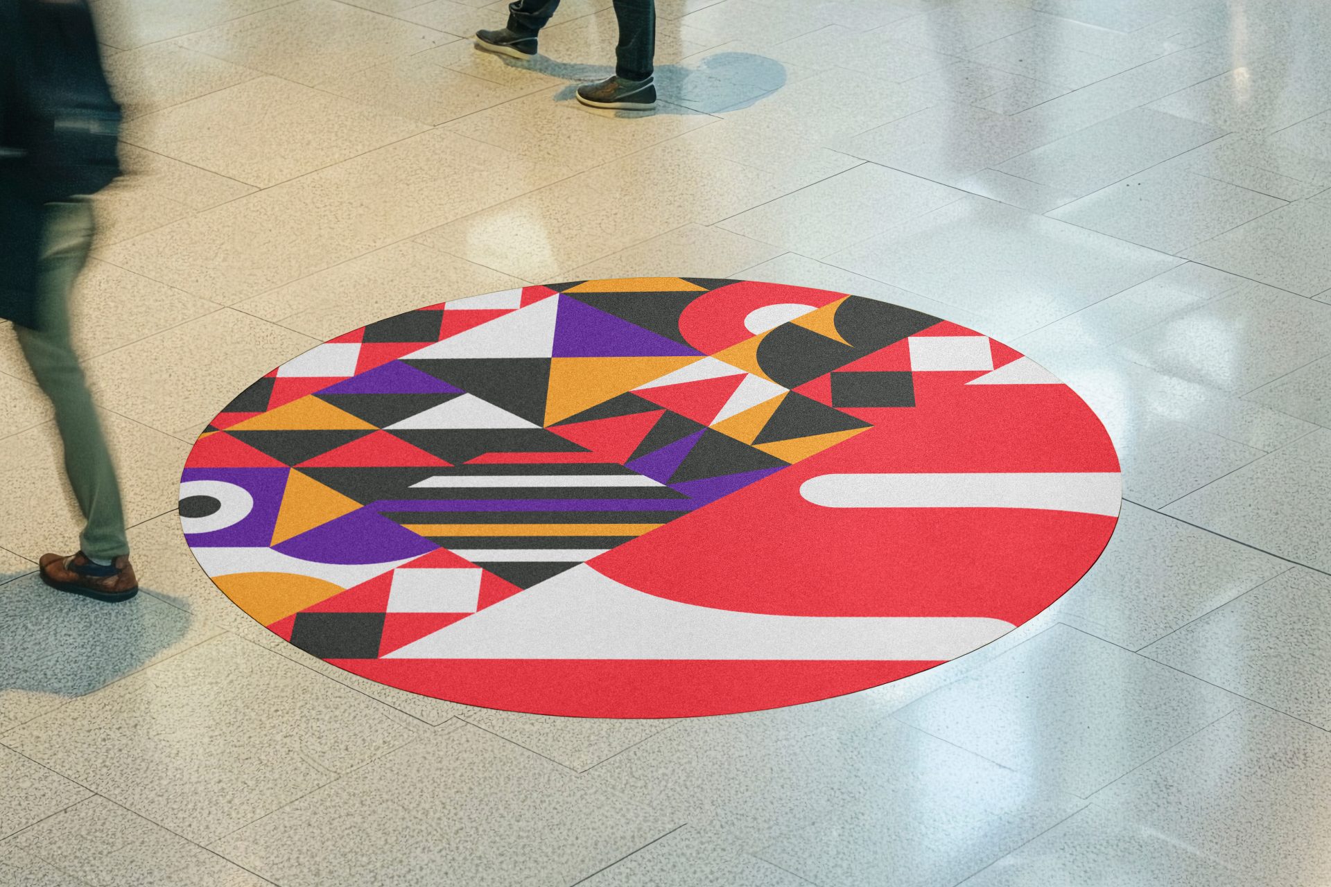 Oval floor vinyl graphic with a bold geometric pattern in red, orange, purple and black, printed and applied to a tiled floor